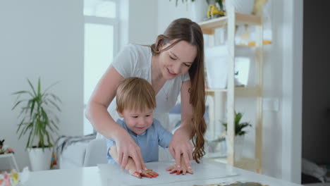 Mamá-Ayuda-A-Su-Hijo-A-Hacer-Una-Huella-En-Papel-Usando-Pintura.-Asunto-De-Ocio-Conjunto-Del-Niño.-Mamá-Feliz-Y-Cariñosa