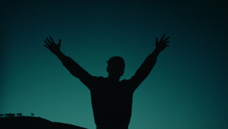 silhouette-of-man-with-arms-raised-celebrating-freedom-on-rooftop-at-twilight-enjoying-independent-lifestyle-looking-at-early-morning-view-of-city-skyline