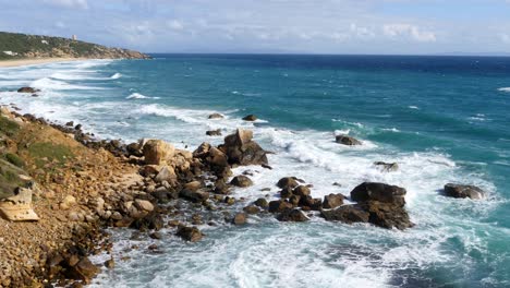 Phare-de-Camarinal,-Lighthouse-Camera-=-Static-shot-of-waves-coming-in-over-rocks-taken-from-Melia-Atlanterra-towards-the-lighthouse