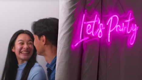 coppia o amici che si divertono in una cabina fotografica con il cartello al neon "let's party" fuori 1