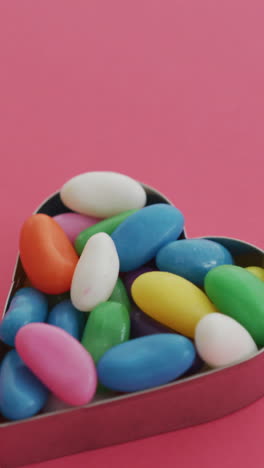 video of overhead view of multi coloured sweets in heart shape over red background