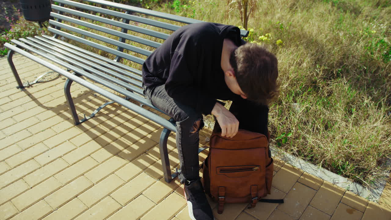 Man Sitting On A Bench In The Nature Searching For Something In The Backpack