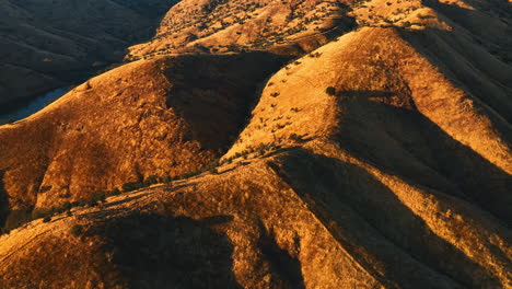 brown rounded tops of california mountains with a lack of greenery growing on. river flowing at the foot of a mount. aerial view.