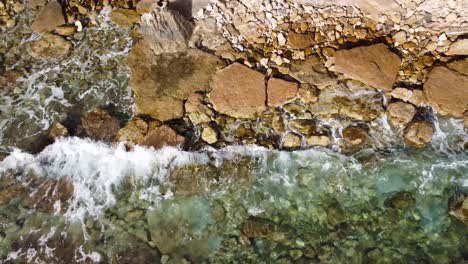 Aerial-Drone-View,-Birds-Eye-looking-down,-Rocky-Mediterranean-Shoreline-in-Calpe,-Spain:-Waves-Crashing-on-Crystal-Clear-Waters