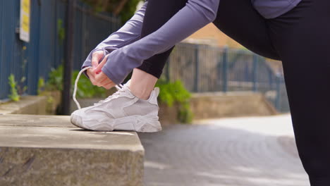 close up of woman tying laces on training shoe before exercising running along urban street 1