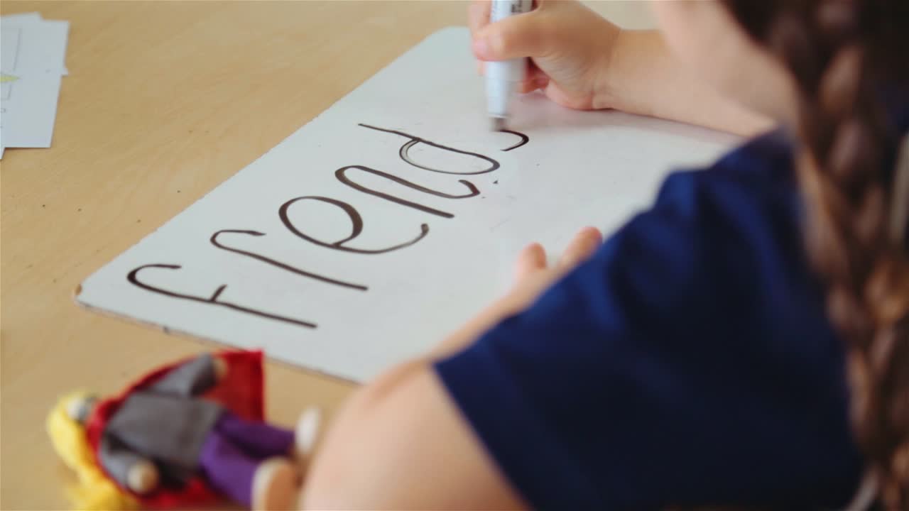 Young girl child writing friends wrong spelling on whiteboard. Handheld Shot. Close up.