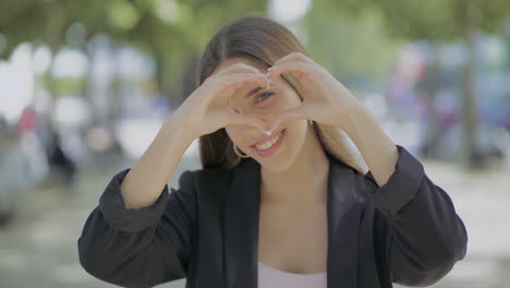 Girl-showing-hand-heart-and-smiling-at-camera