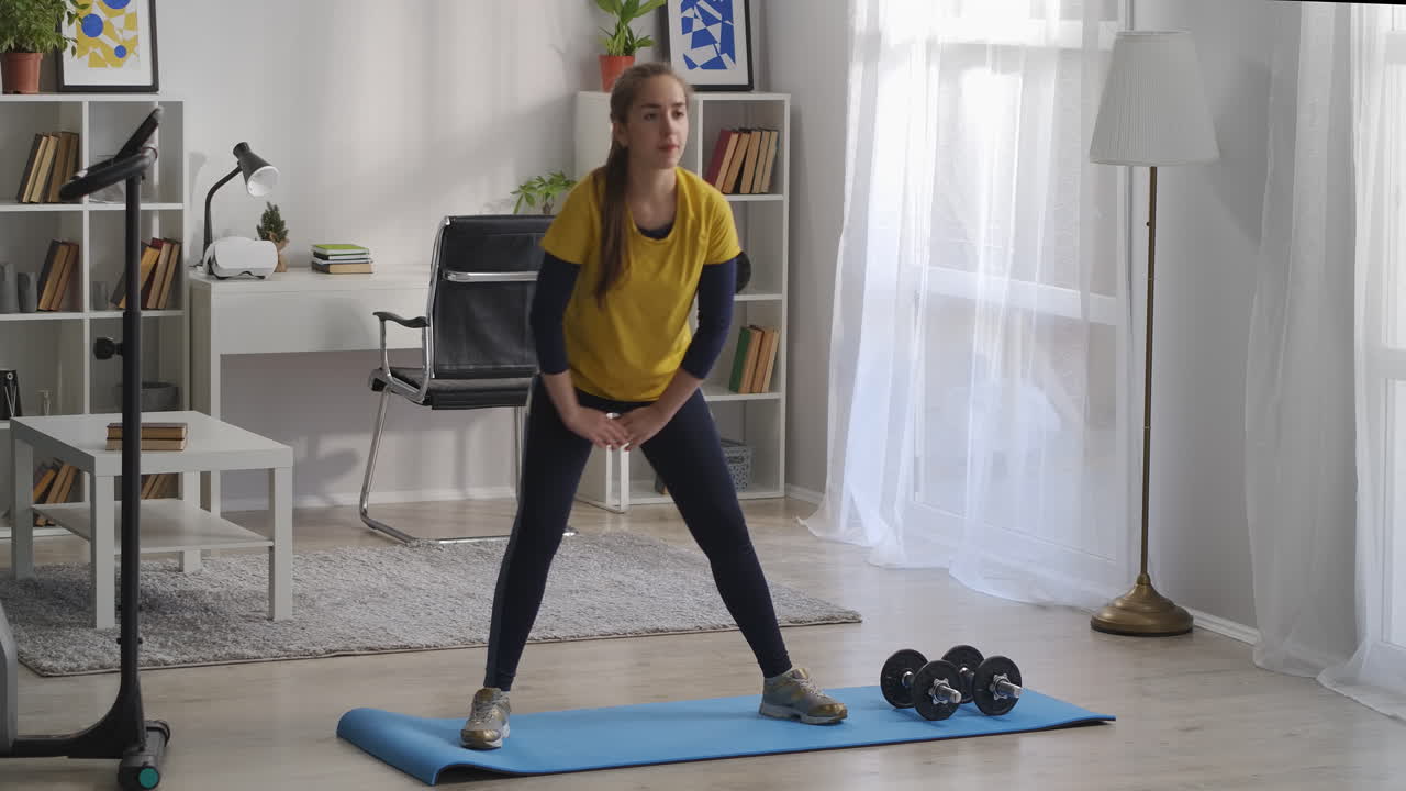 una adolescente deportiva está haciendo ejercicios para las piernas en la sala de estar en cuclillas en los lados y tensando los músculos de las caderas helathy estilo de vida y actividades deportivas