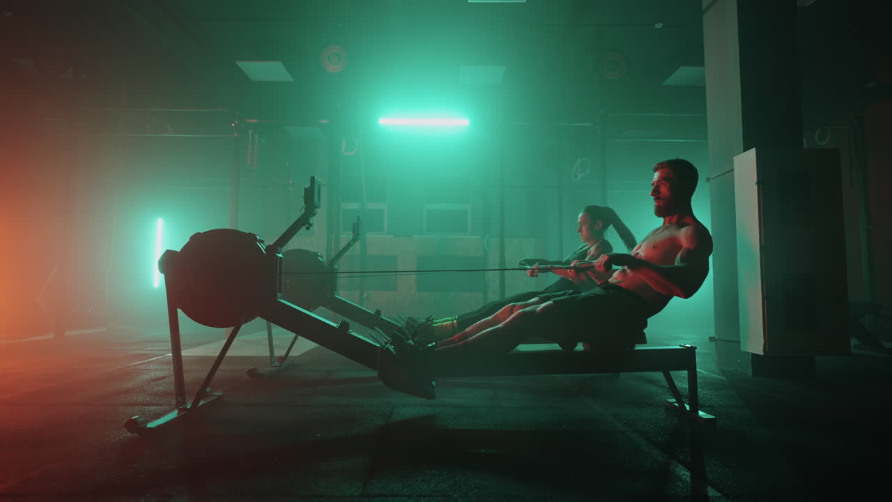 A man and a woman perform strong athletes perform exercises in the gym on a rowing machine in slow motion