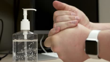 a pair of caucasian hands pressing down on a hand sanitizer bottle dispensing a measure of liquid onto the hands as the hands then applying it