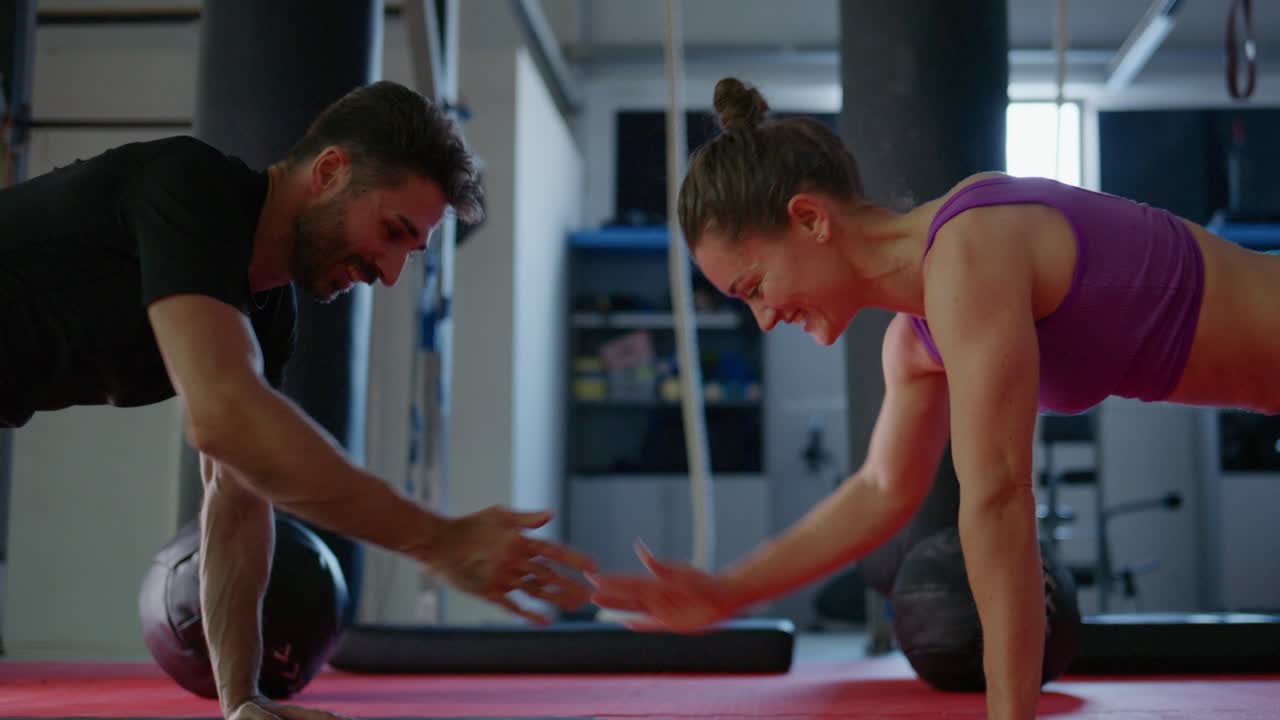 Sesión de entrenamiento dinámico: pareja haciendo flexiones, mostrando trabajo en equipo, fuerza y determinación en un entorno de gimnasio moderno con equipamiento de fitness