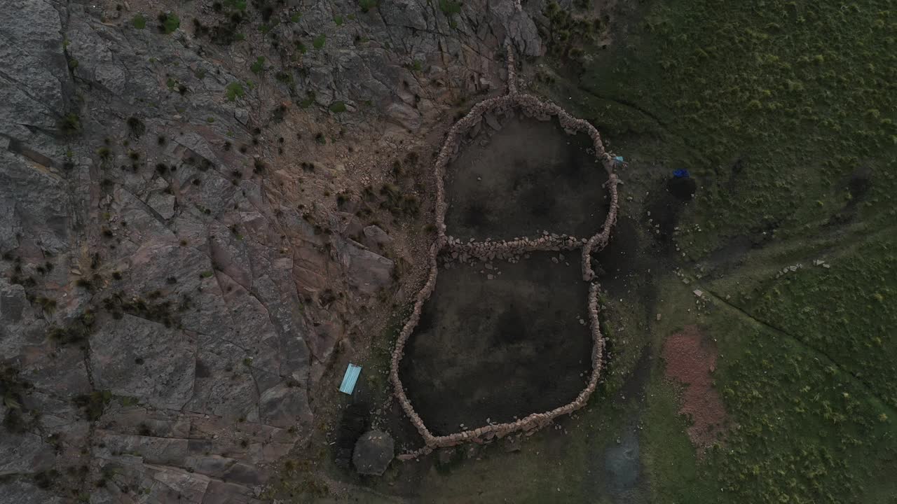 vista aérea superior sobre una pequeña cabaña rodeada de muros de piedra junto a las granjas de terrazas incas en los andes bolivianos con un estrecho cañón al lado