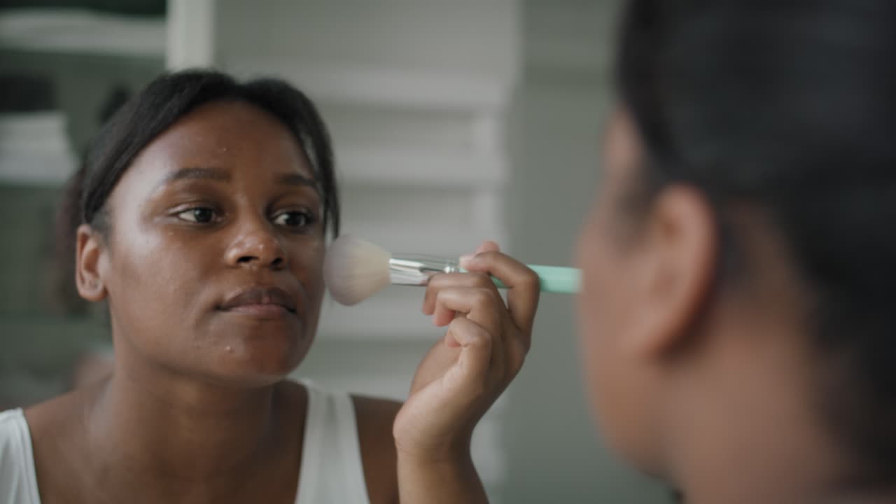 mujer afroamericana aplicando maquillaje en el baño.