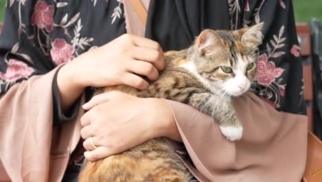 woman holding a cat in her arms wearing a brown abaya