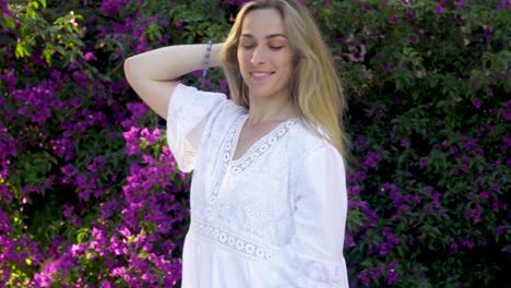 Portrait-of-the-attractive-blonde-woman,-playing-with-her-hair-and-posing-to-the-camera-in-the-background-of-purple-flowers