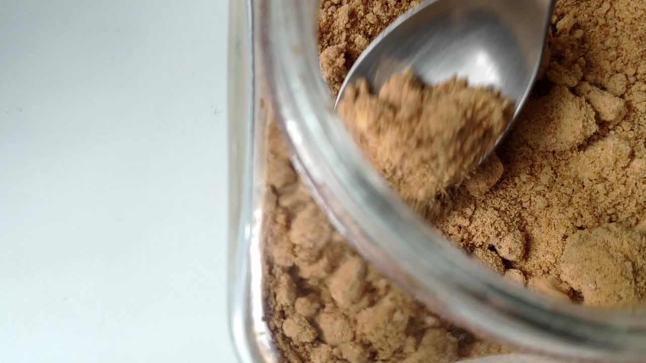 Brown raw cane sugar in a glass jar, close-up shot showing granules and texture