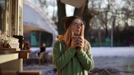 mujer alegre bebiendo una bebida caliente, vapor de café o té caliente en el parque de la ciudad