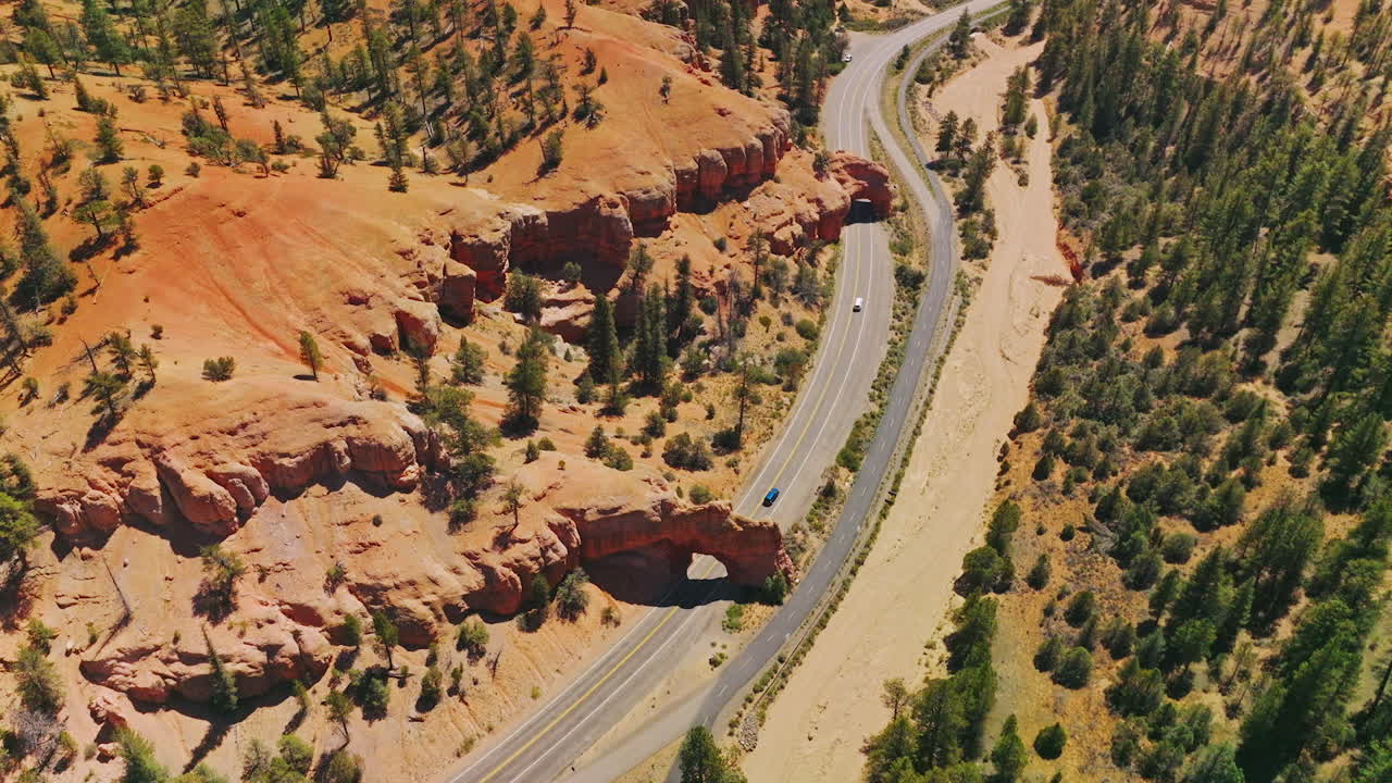 Cars going under the rock arches on the highway in National Park. Sunny daytime footage over the Arches canyons, Utah, USA.