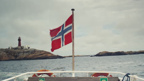 the norwegian flag blowing in the wind on the back of a medium sized boat