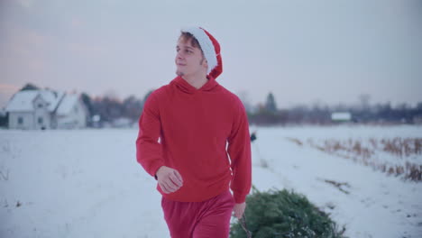 Hombre-Sonriente-Tirando-De-Trineo-Con-árbol-De-Navidad-En-El-Paisaje-Cubierto-De-Nieve-Durante-La-Puesta-De-Sol.