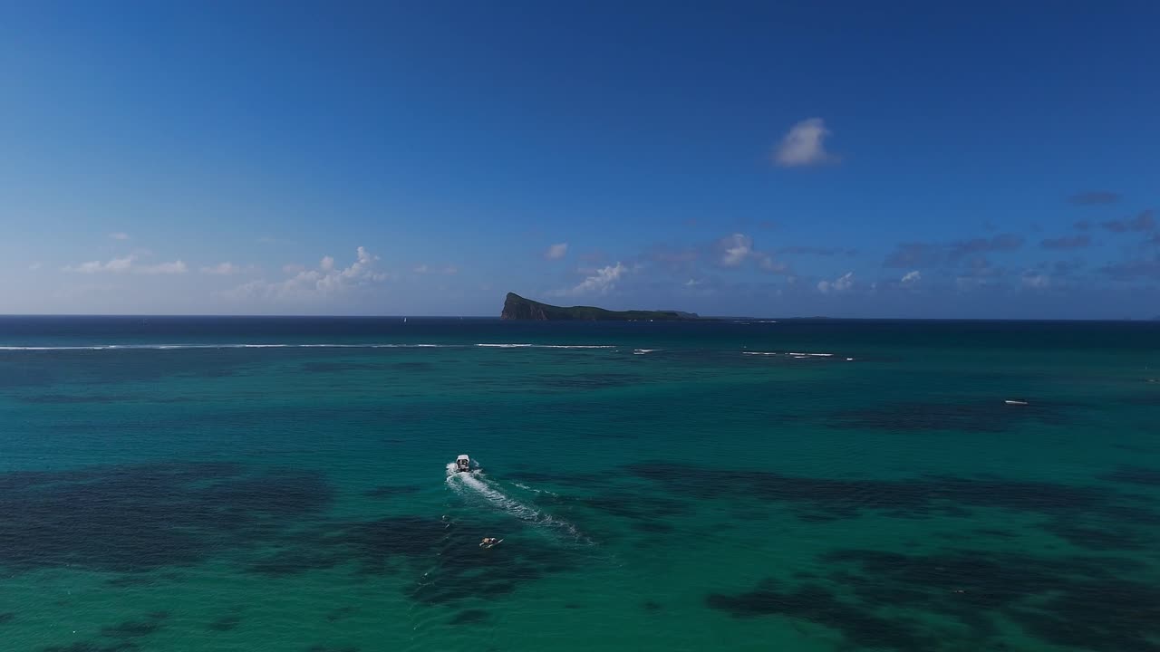 Aerial view of a boat cruising towards Coin de Mire Island, Mauritius, surrounded by vibrant turquoise waters. Ideal for travel, adventure, marine life, and island exploration concepts.
