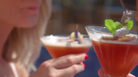 Unrecognizable-couple-enjoying-refreshing-drinks-lying-on-sunbeds-on-poolside