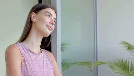 Caucasian-young-woman-looking-out-window,-wearing-pink-tank-top,-copy-space