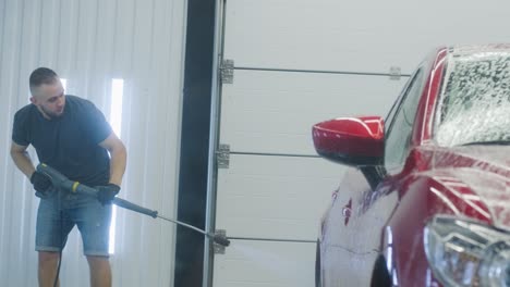 man worker washing red car on a car wash.