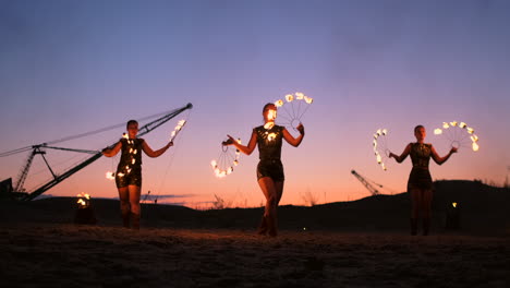 Fire-show-three-women-in-their-hands-twist-burning-spears-and-fans-in-the-sand-with-a-man-with-two-flamethrowers-in-slow-motion