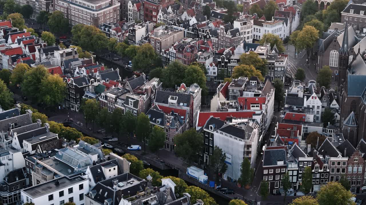 Drone dolly right across Amsterdam city center at golden sunrise, rooftops and canals, city block urban textured backdrop