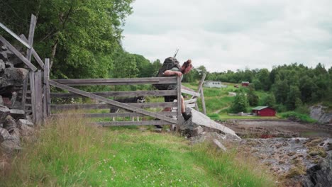 Backpacker-With-Dog-Pet-Alaskan-Malamute-Making-Way-Through-Wooden-Fence-In-Norwegian-Countryside