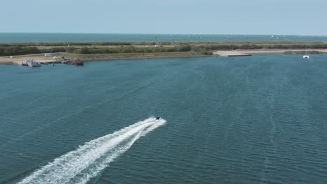 drone - aerial shot of a jetski on a blue, wavy and windy sea on a sunny day with white clouds on a island, 30p