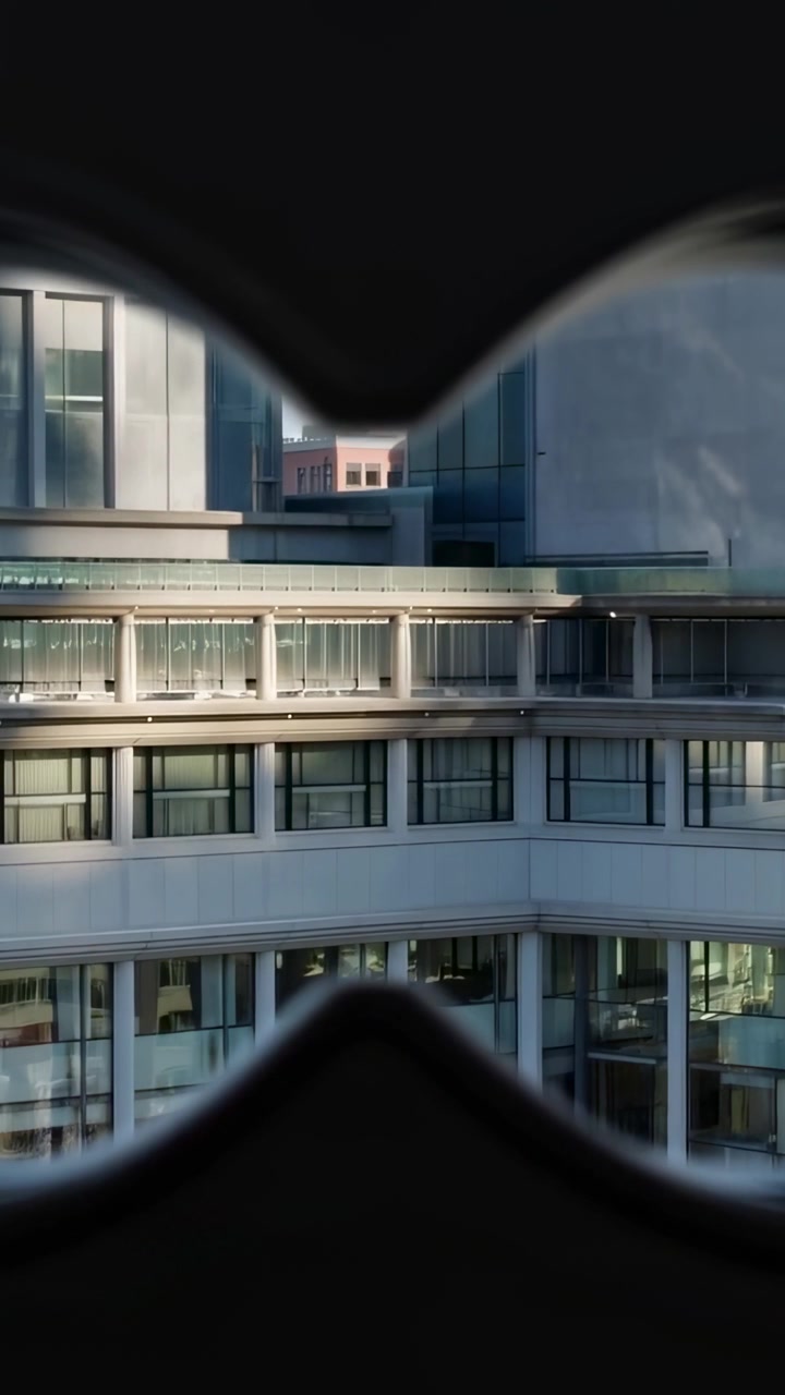 Video verticale: Mentre la telecamera si sposta, una facciata con elementi che ricordano occhiali che rivela mattoni rosa in un vicolo.