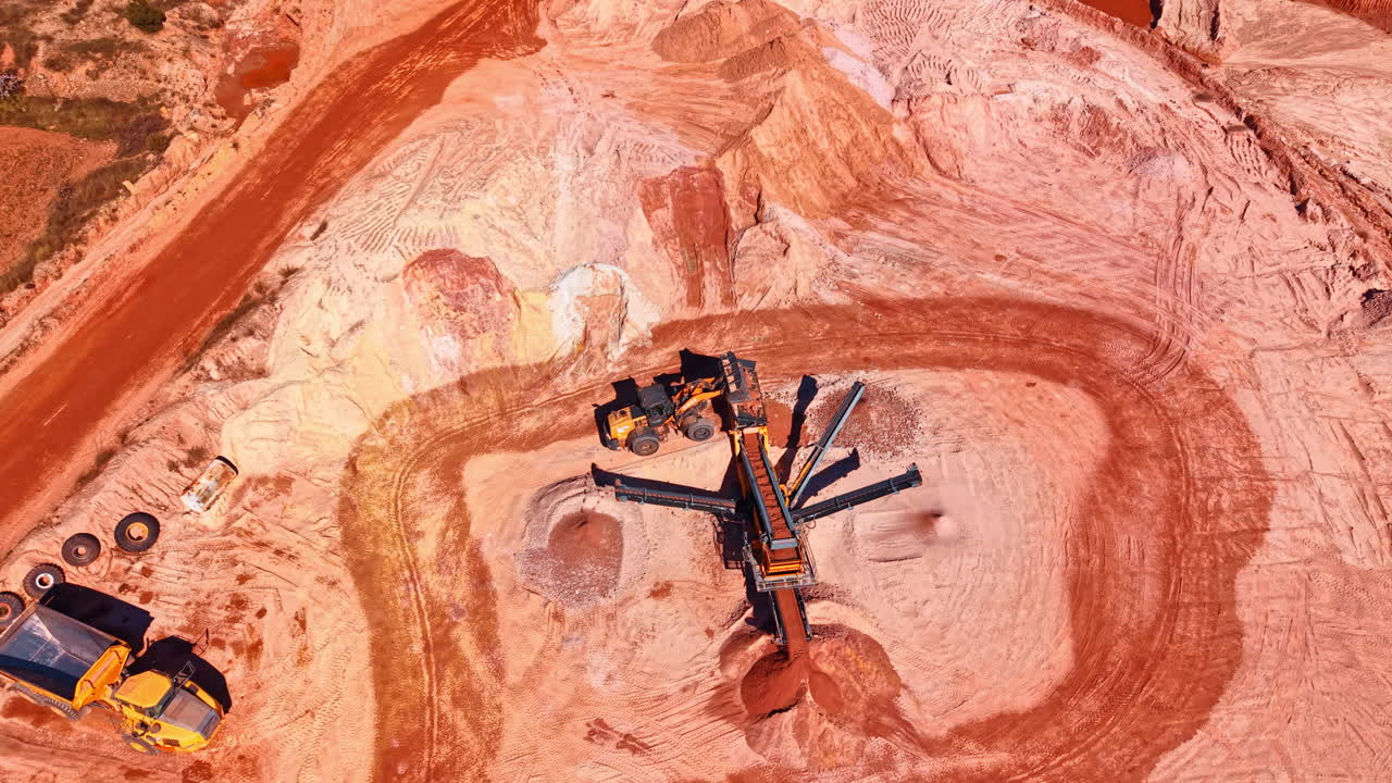 Madrid, Spain, 8 August 2025: Top down view of mobile crushing plant in quarry. Bird's-eye view of industrial machinery, conveyor belts, and a loader working with red clay and stone extraction
