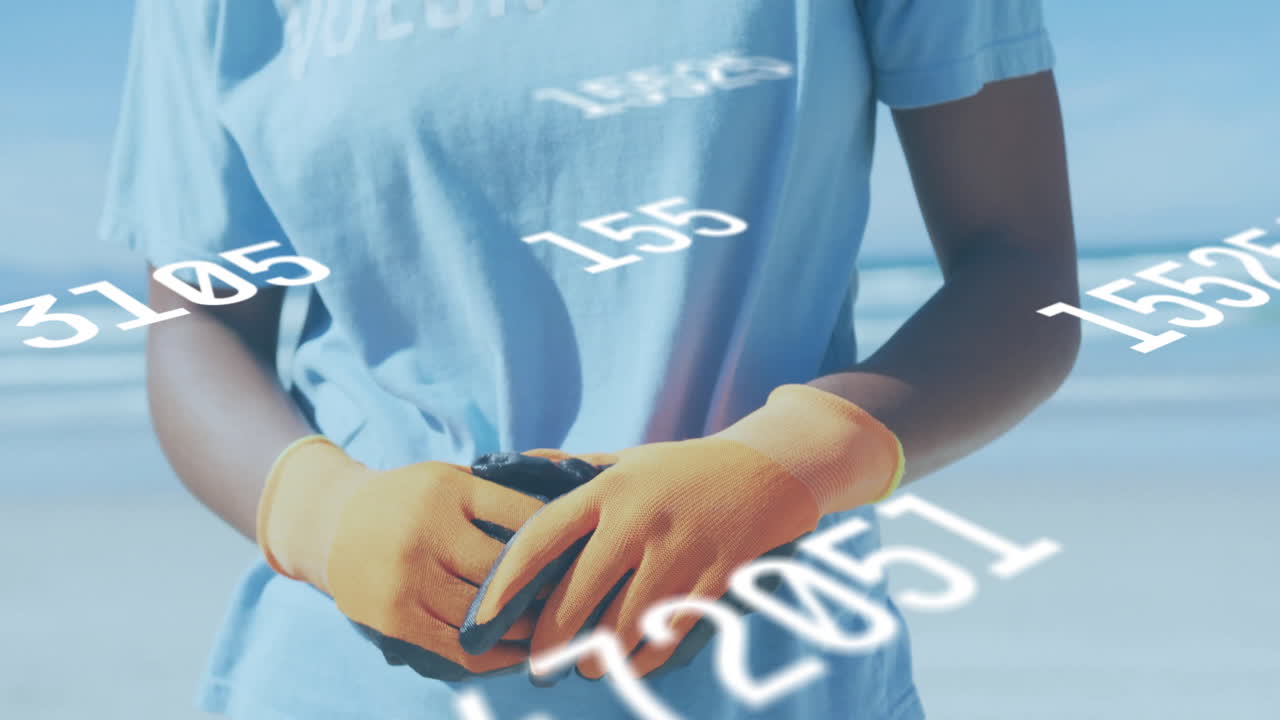 Person wearing VOLUNTEER shirt with floating numbers animation over beach background