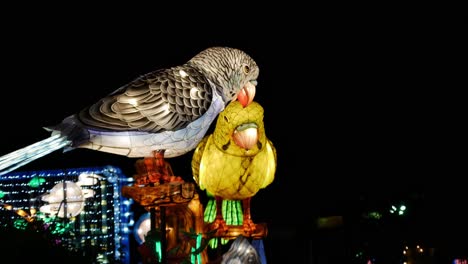 two light animatronic parrots move their winds and beaks against a dark night sky