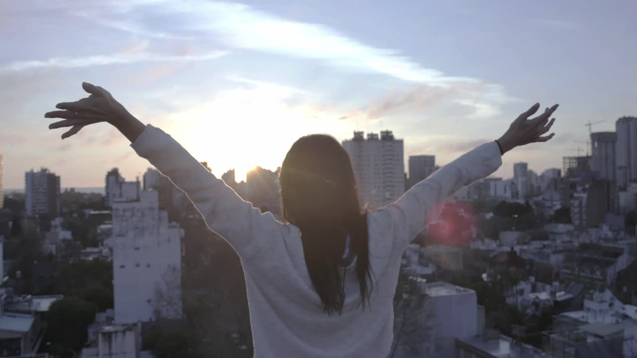 Giovane donna con le braccia tese che ammira lo skyline della città al tramonto