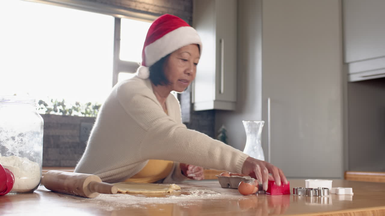 Senior Asian woman in Santa hat baking Christmas cookies at home, feeling joyful