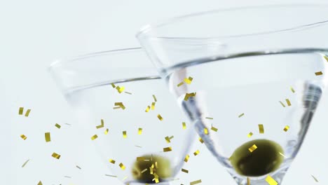 Golden-confetti-falling-over-close-up-of-olives-in-two-cocktail-glasses-against-grey-background