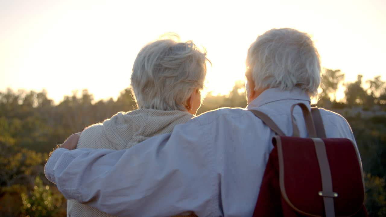夕暮れを眺めるハイキング中の上級夫婦の後ろの景色