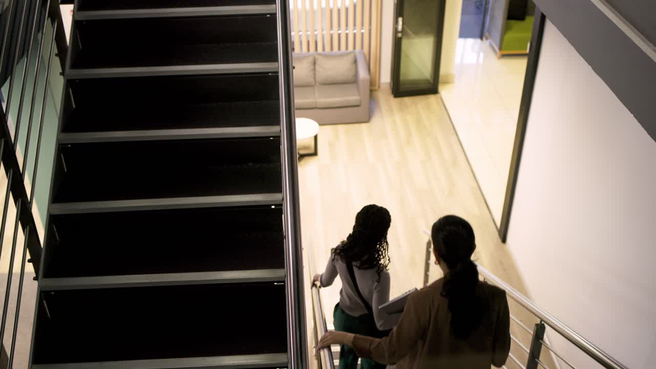 Al llegar a las escaleras, compañeros de trabajo diversos con portátil bajando hacia la zona de descanso de la oficina, espacio para texto