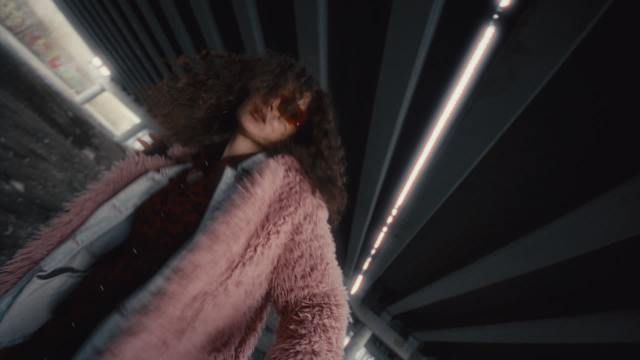 Girl in Fur Coat and Sunglasses Dancing Energetically under Urban Overpass