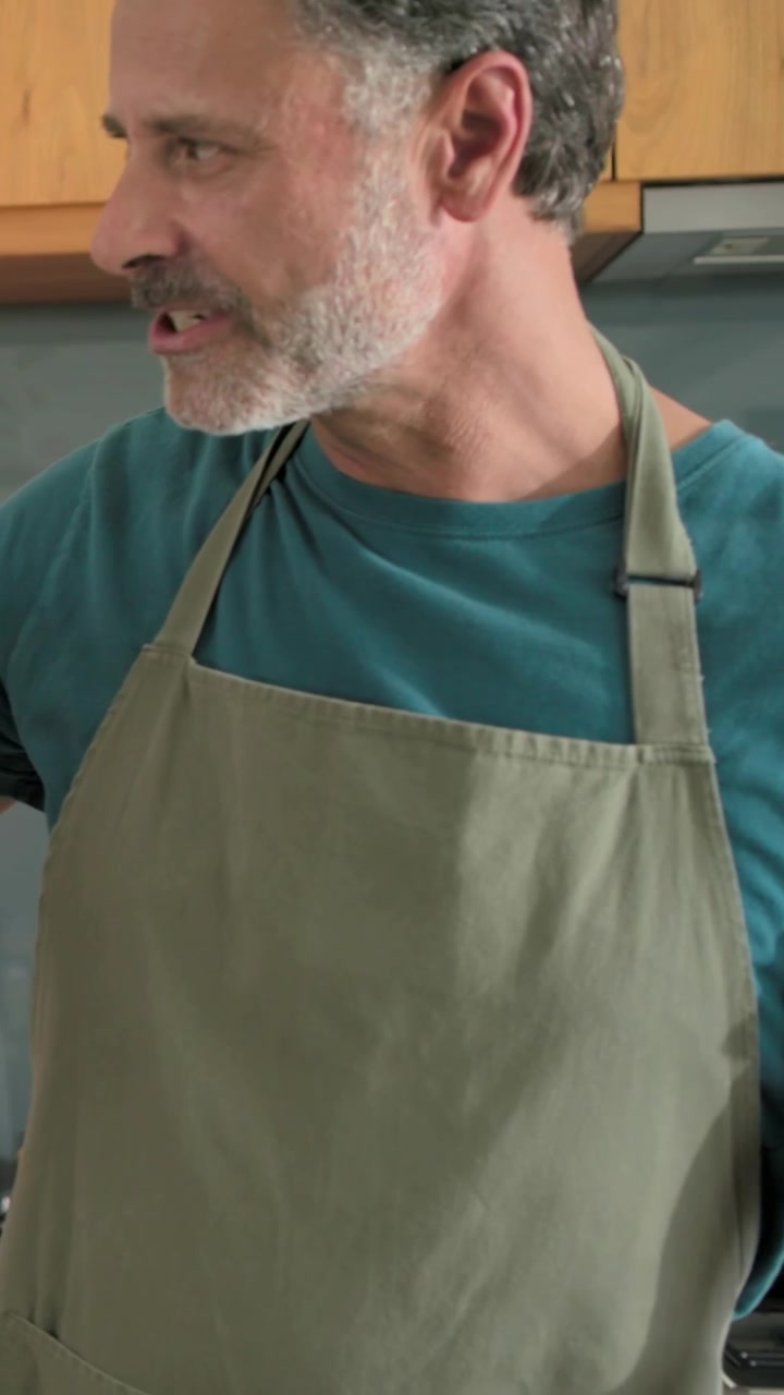 Vertical video: Placing 2nd wine glass woman in sage apron calling man slicing cucumber for meal