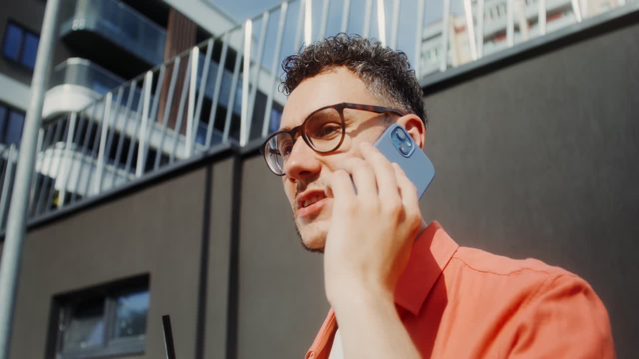 남자가 야외에서 음료를 마시면서 전화로 얘기하고 있습니다.