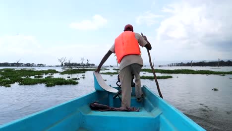 Afrikanischer-Mann,-Der-Mit-Einem-Stock-In-Einem-Blauen-Faserboot-Rudert,-Das-Crescent-Island,-Kenia-Verlässt