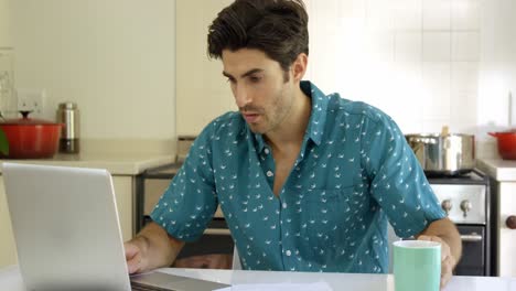 hombre usando una computadora portátil y escribiendo en el papel en la cocina