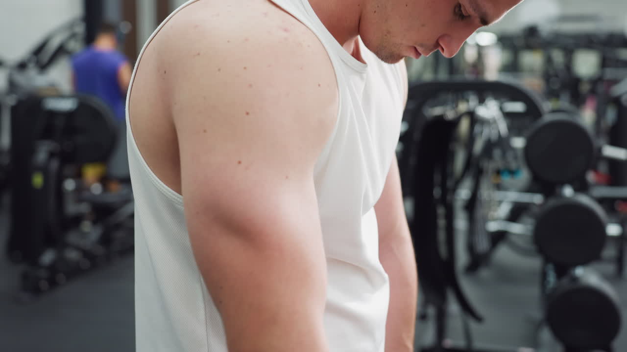 Gym goer shakes hands vigorously to loosen muscles before cable machine workout, white singlet and black shorts visible, modern fitness environment with weights and machines in soft focus background