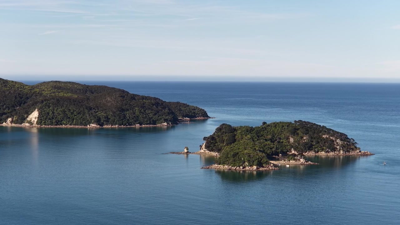 Naturskøn droneudsigt over små skovklædte øer og stille blåt hav langs New Zealands Sydøs kystlinje, en natur- og afslapningsudsigt.