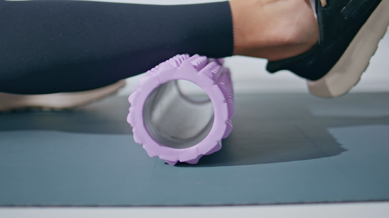 Closeup sportswoman using massaging roller doing fitness workout in light gym