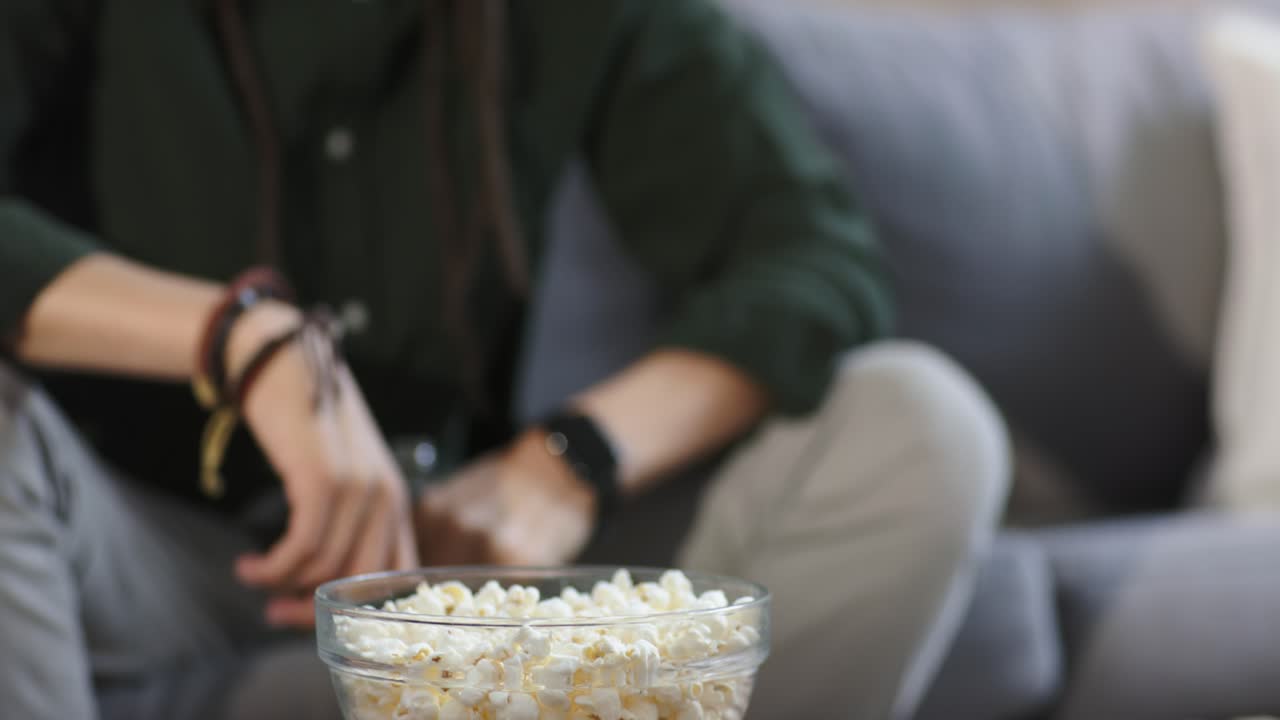 Homem a esticar-se para pegar numa garrafa na mesa, a desenroscar a tampa, a pegar no comando e a ajustar o volume da TV.